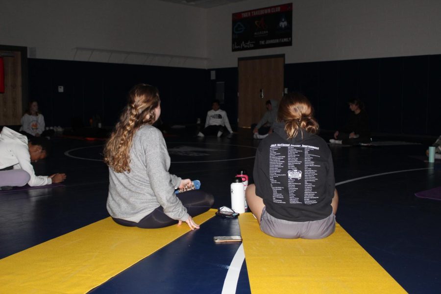 Two yoga students sit on yoga mats during class. 